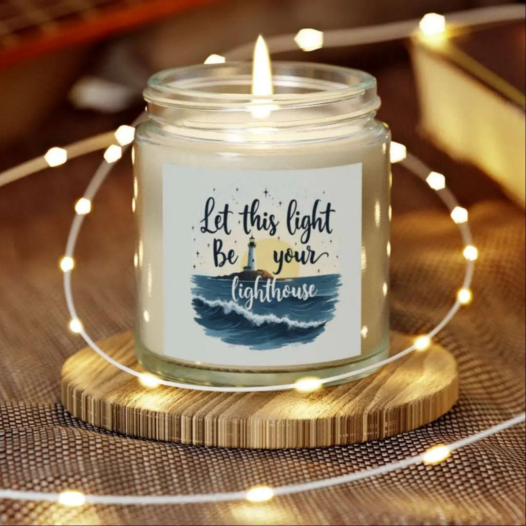 A 4 oz clear jar scented candle featuring a lighthouse with the sun and the phrase 'Let this Light Be Your Lighthouse.' A calming and inspirational candle, perfect for coastal decor.