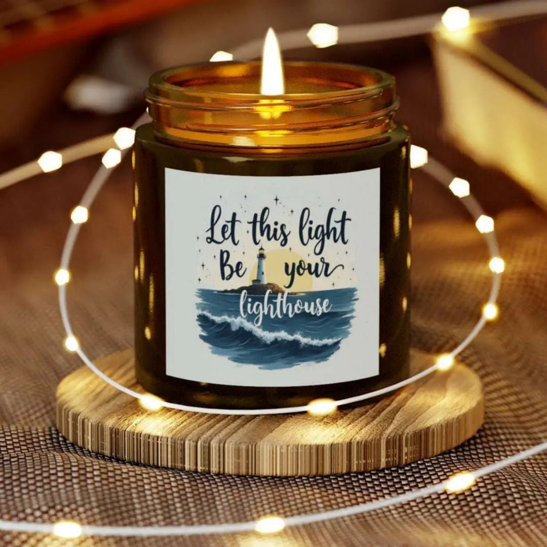 A 4 oz amber jar scented candle featuring a lighthouse with the sun and the phrase 'Let this Light Be Your Lighthouse.' A calming and inspirational candle, perfect for coastal decor.