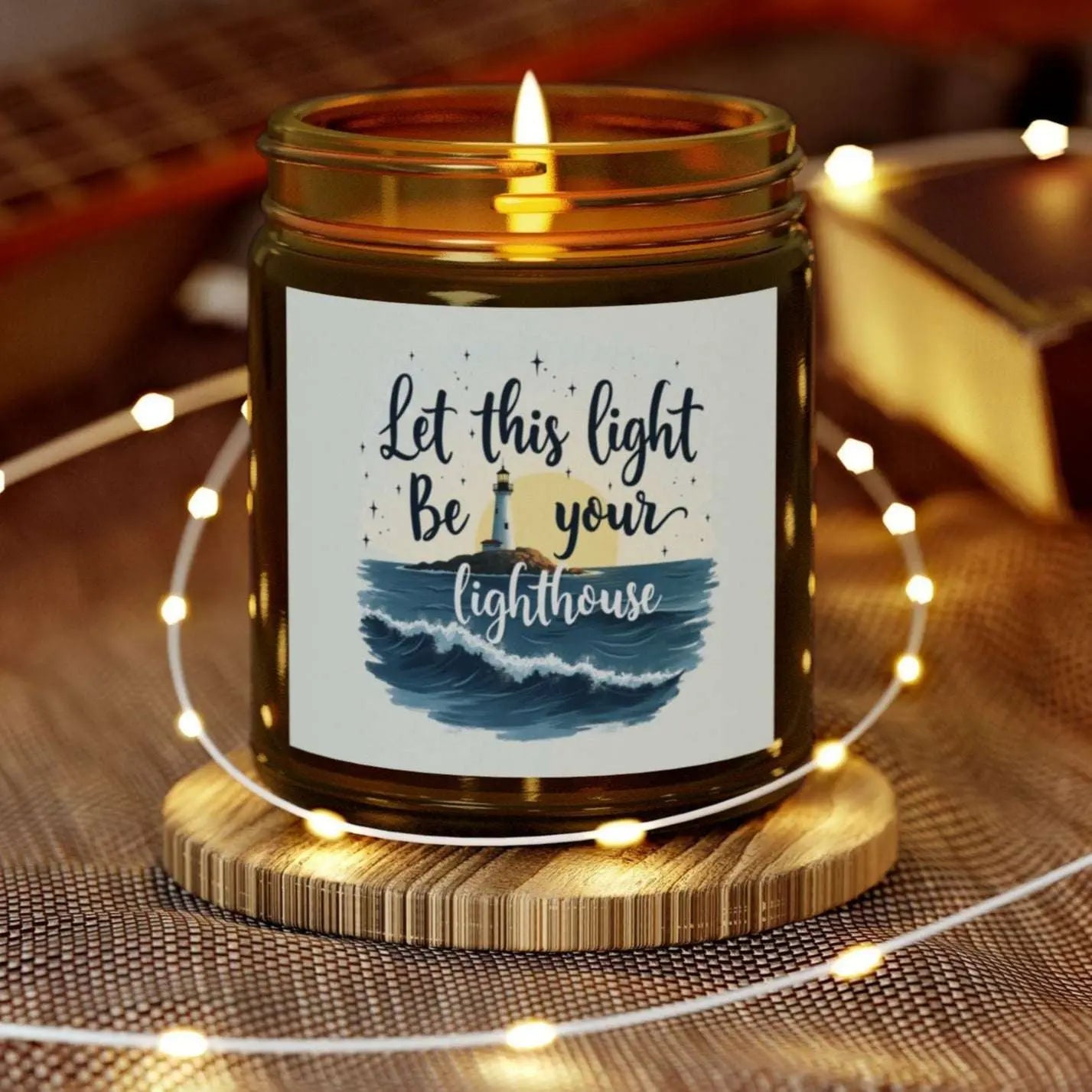 A 9 oz amber jar scented candle featuring a lighthouse with the sun and the phrase 'Let this Light Be Your Lighthouse.' A calming and inspirational candle, perfect for coastal decor.