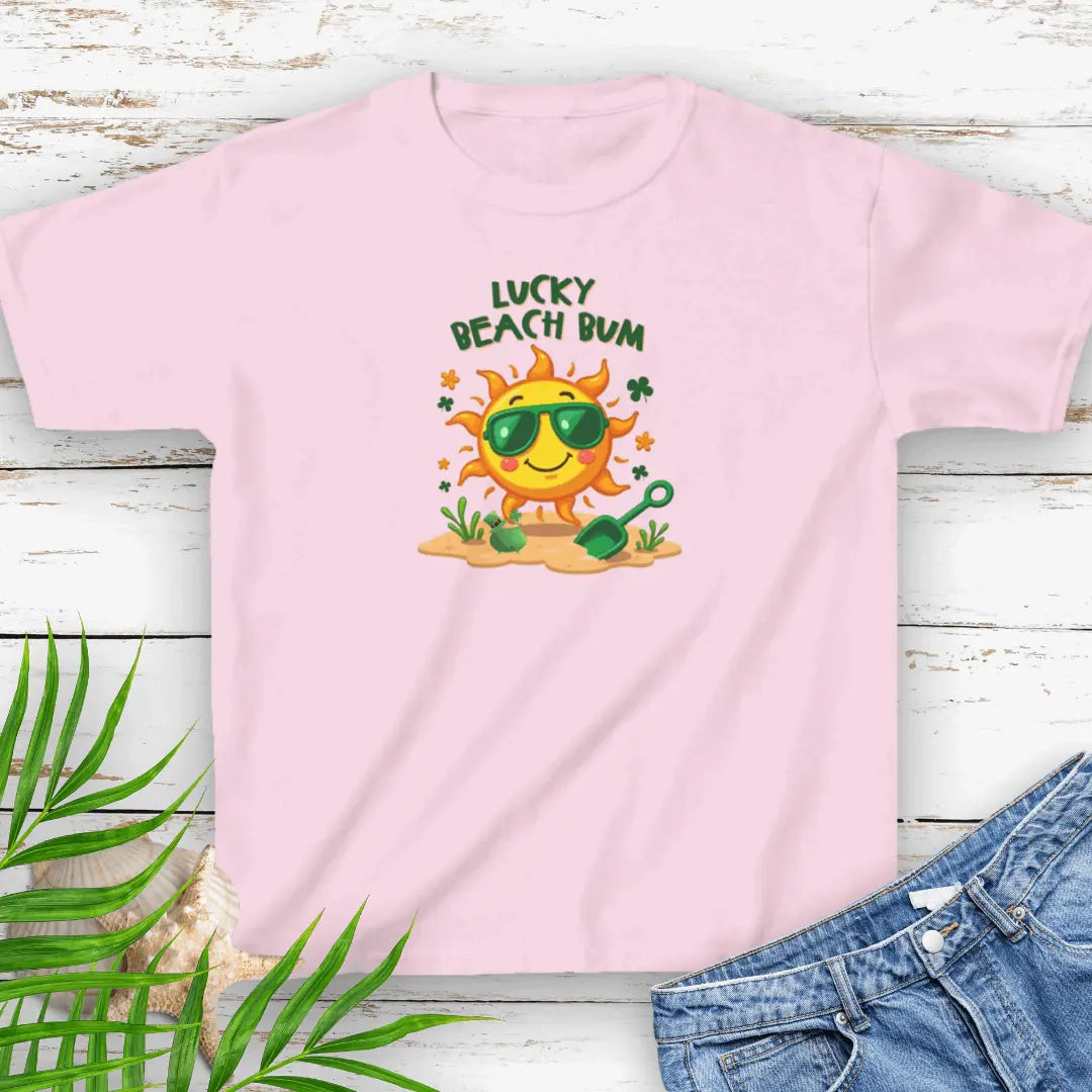 Lucky Beach Bum Child's Pink small T-shirt with a smiling sun wearing green sunglasses on the beach with beach toys.