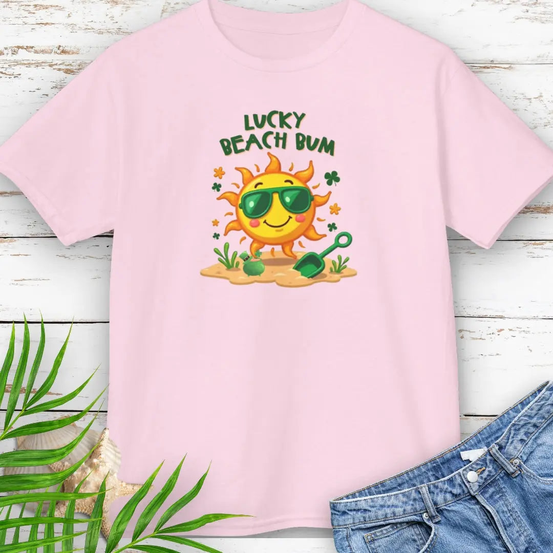 Lucky Beach Bum Child's Pink T-shirt with a smiling sun wearing green sunglasses on the beach with beach toys.
