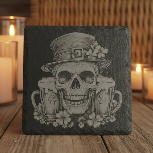 Slate coaster with a skull design wearing a top hat and holding beer mugs, surrounded by flowers on a wooden surface.
