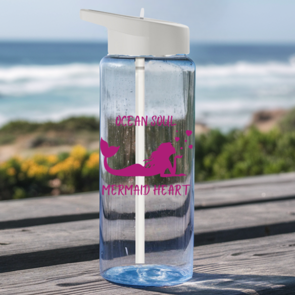 Clear Water bottle with gray lid and straw with a mermaid that says Ocean Soul Mermaid Heart sitting on a picnic table at the beach