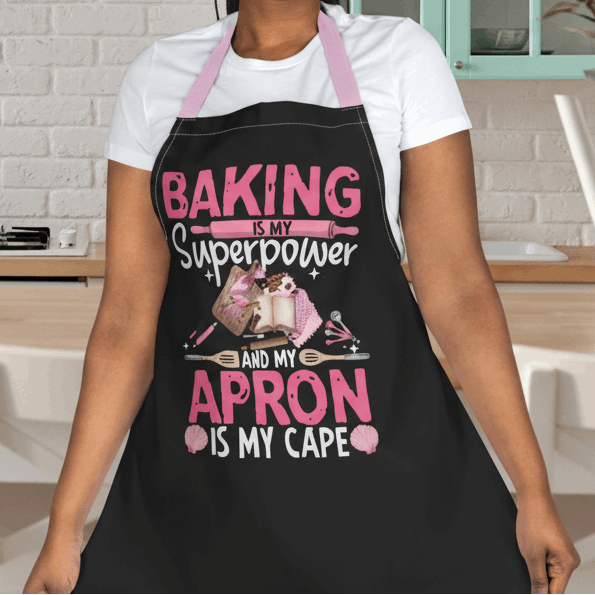 Person wearing a black apron with baking elements and text 'Backing is my Superpower and my Apron is my cape.