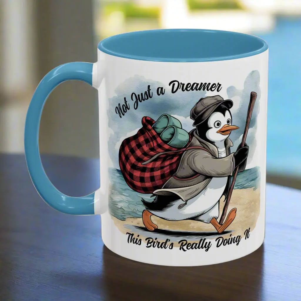 White 11 oz  coffee mug with a light blue interior and handle featuring a fun beach design of a penguin running away on the sand with the text 'Not Just a Dreamer, This Bird’s Really Doing It.' A playful and unique gift for beach lovers and dreamers.