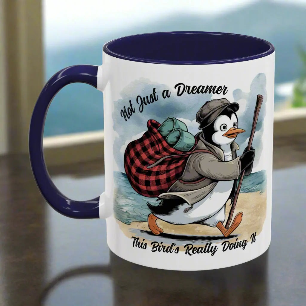 White 11 oz coffee mug with a navy blue interior and handle featuring a fun beach design of a penguin running away on the sand with the text 'Not Just a Dreamer, This Bird’s Really Doing It.' A playful and unique gift for beach lovers and dreamers.