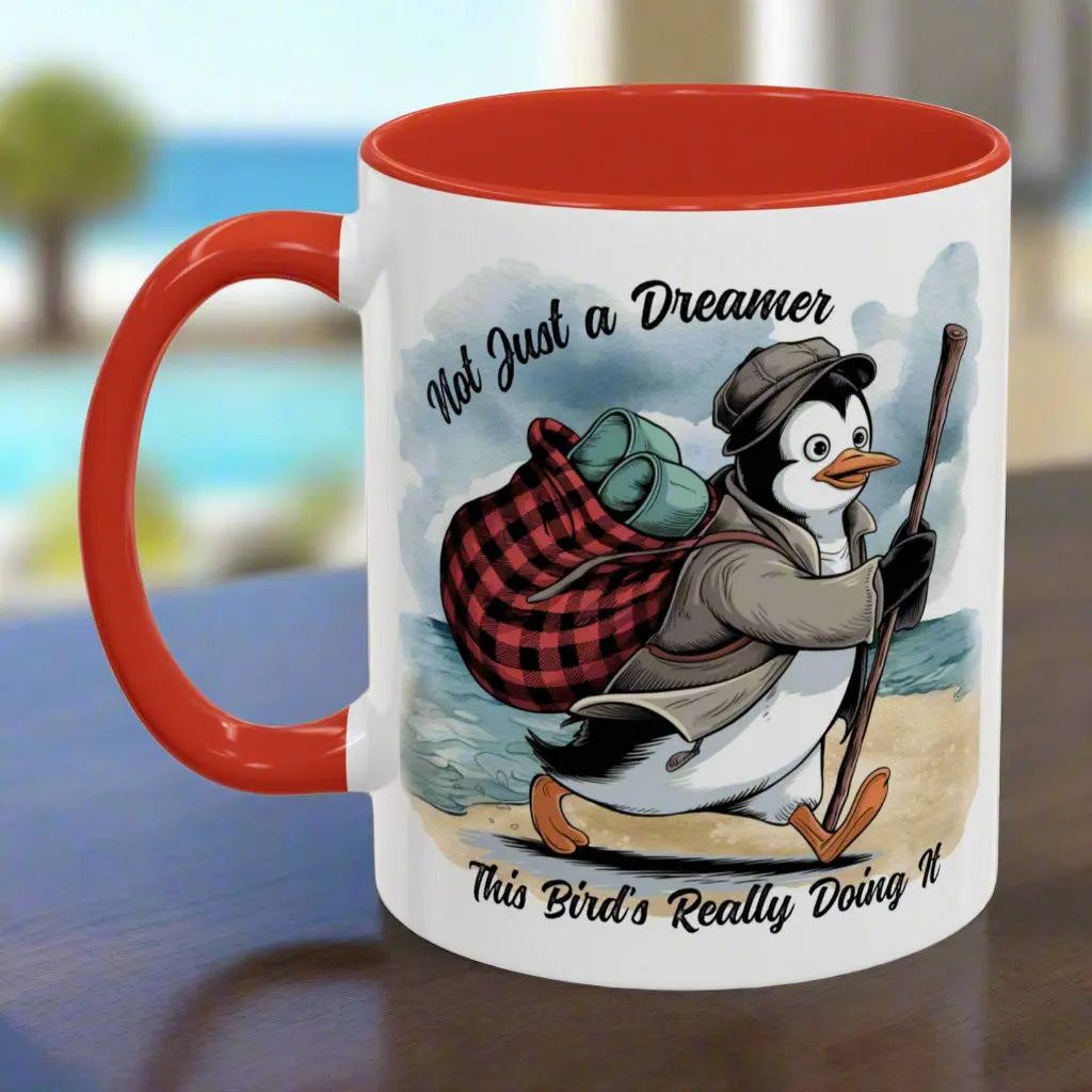 White 11 oz coffee mug with red interior and handle featuring a fun beach design of a penguin running away on the sand with the text 'Not Just a Dreamer, This Bird’s Really Doing It.' A playful and unique gift for beach lovers and dreamers.