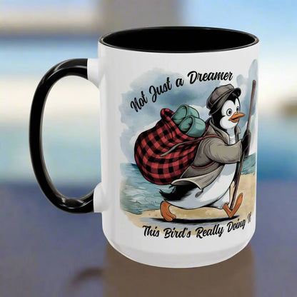 White 15 oz coffee mug with black interior and handle featuring a fun beach design of a penguin running away on the sand with the text 'Not Just a Dreamer, This Bird’s Really Doing It.' A playful and unique gift for beach lovers and dreamers.