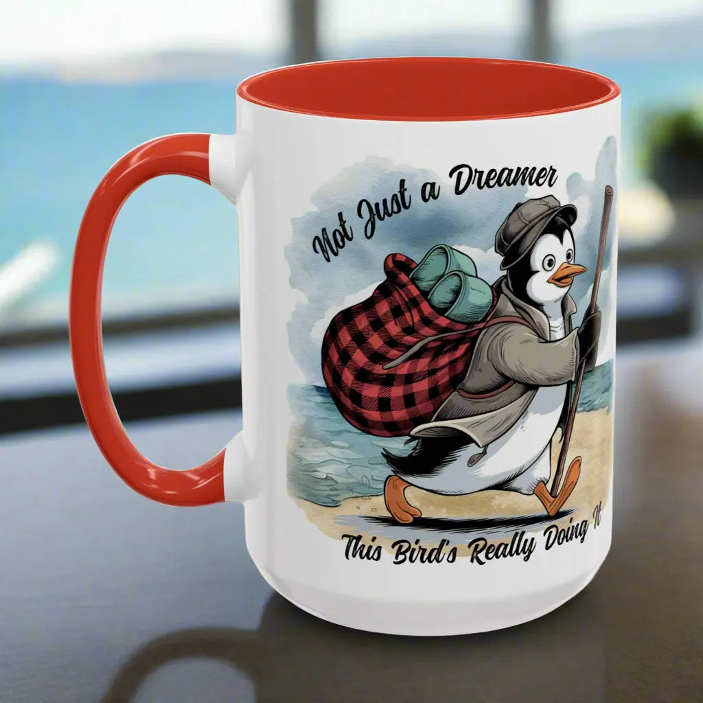 White 15 oz coffee mug with red interior and handle featuring a fun beach design of a penguin running away on the sand with the text 'Not Just a Dreamer, This Bird’s Really Doing It.' A playful and unique gift for beach lovers and dreamers.