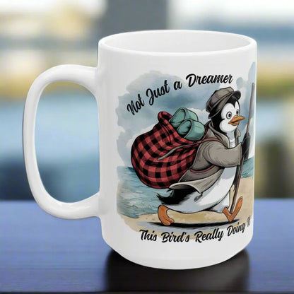 White 15 oz coffee mug featuring a fun beach design of a penguin running away on the sand with the text 'Not Just a Dreamer, This Bird’s Really Doing It.' A playful and unique gift for beach lovers and dreamers.