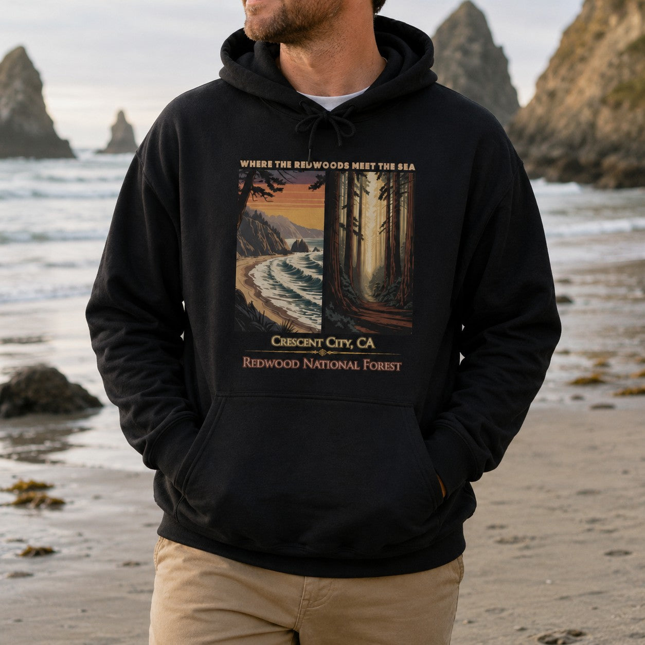 A man wearing a black Crescent City California hoodie featuring vintage redwood forest and Pacific coast artwork with Where the Redwoods Meet the Sea design.