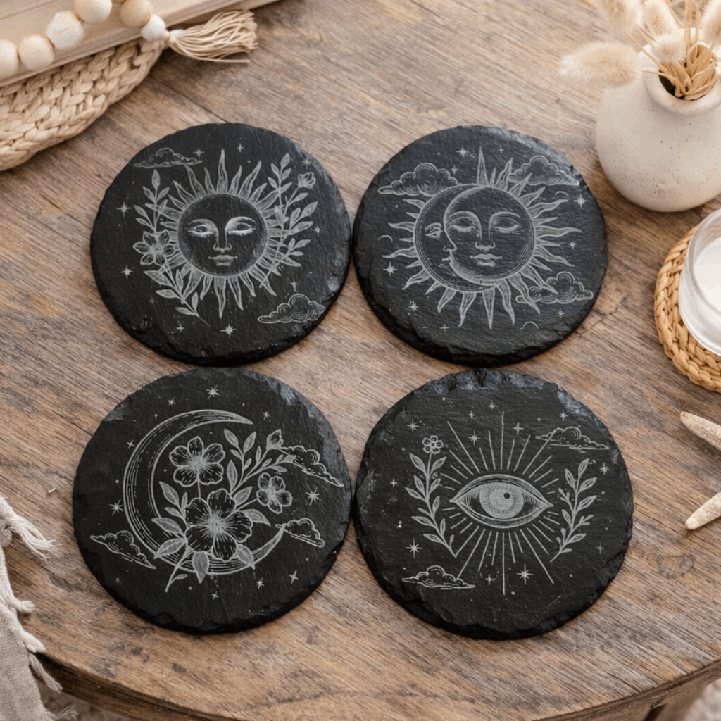 Four black stone coasters with celestial designs on a wooden table.