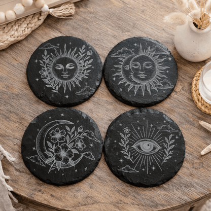 Four black stone coasters with celestial designs on a wooden table.