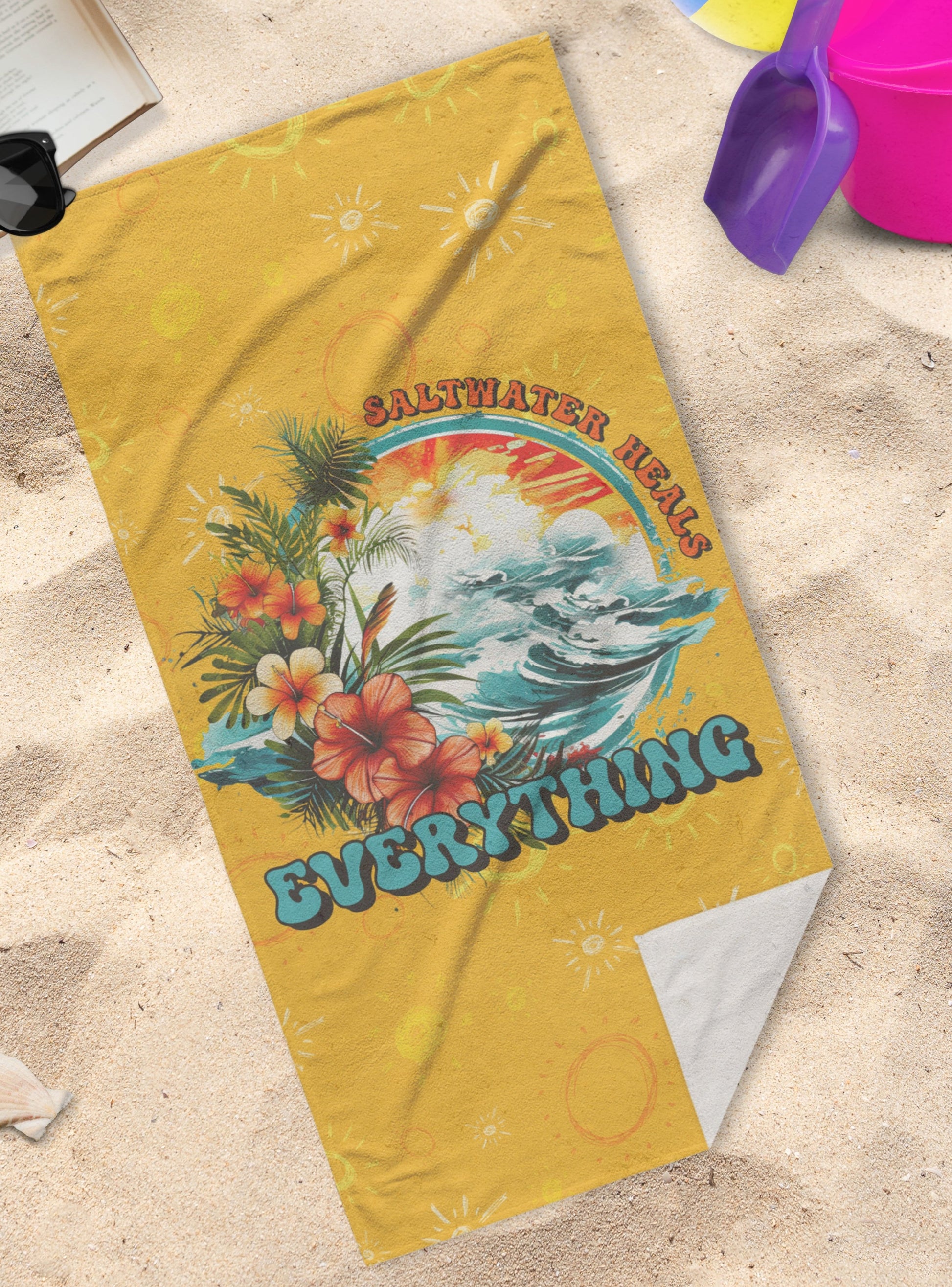 Bright yellow towel with a picture of waves with tropical flowers that says Saltwater Heals Everything around the side of the image