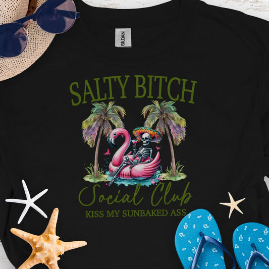 Black t-shirt beach skeleton floating in flamingo floaty between two palm trees with text Salty Beach Social Club Kiss my sunkissed ass.