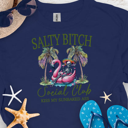 Navy t-shirt beach skeleton floating in flamingo floaty between two palm trees with text Salty Beach Social Club Kiss my sunkissed ass.