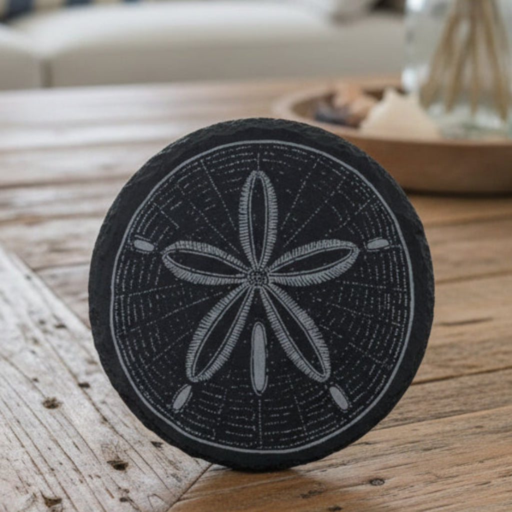 Black slate coaster with sand dollar design engraved.
