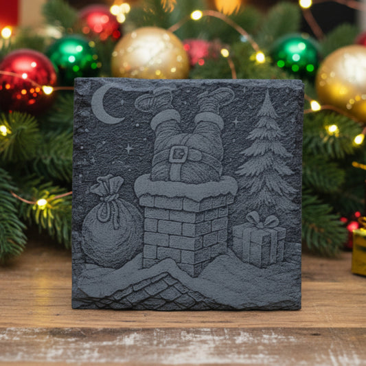 Decorative slate coaster with engraved Christmas scene featuring Santa Claus going down a chimney, and presents on the roof.