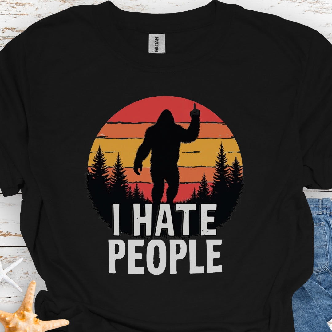 Black t-shirt with sasquatch holding up middle finger walking into retro sunset with black forest with text I hate people.