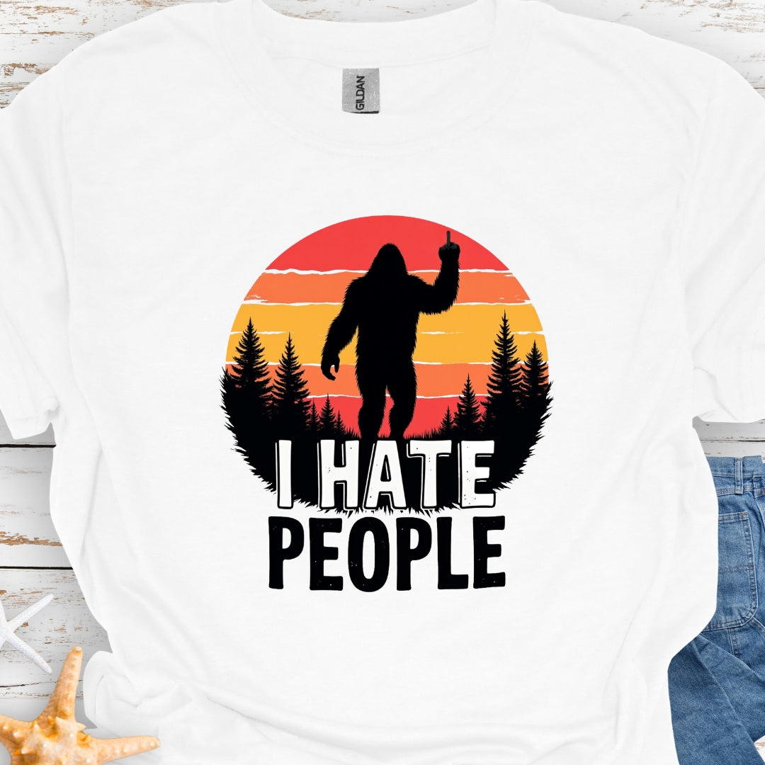 White  t-shirt with sasquatch holding up middle finger walking into retro sunset with black forest with text I hate people.