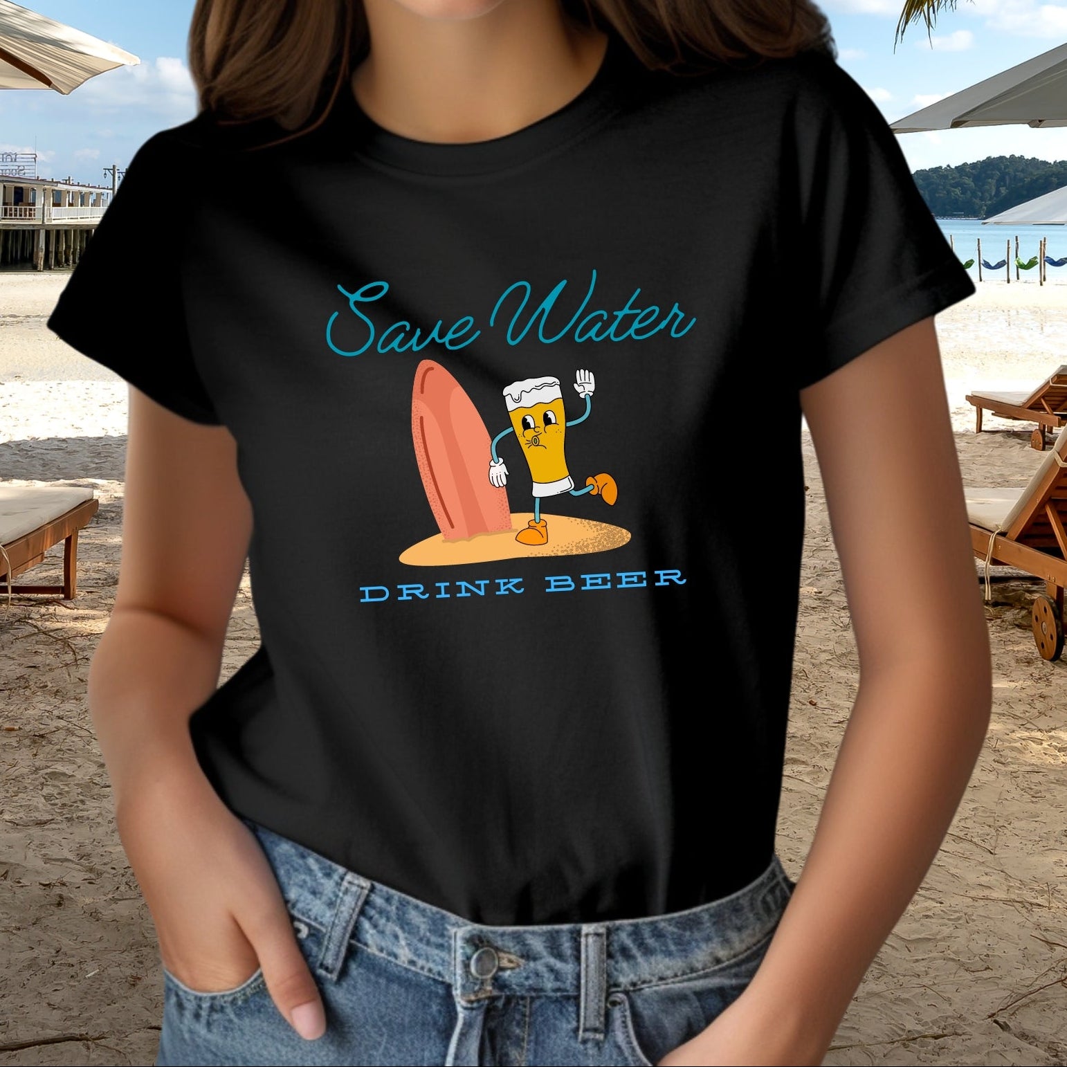 Woman wearing a black t-shirt with a humorous graphic of cartoon pilsner beer mug and surfboard on beach with text Save Water Drink Beer.