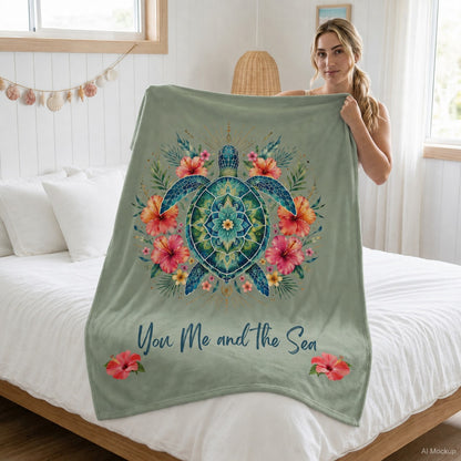 A woman holding a sage green ultra-soft plush blanket featuring a vibrant mandala sea turtle surrounded by tropical hibiscus flowers with the phrase "You, Me and the Sea" on a sage-green background.