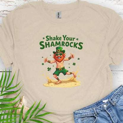 Shop our fun and festive dancing leprechaun in beach attire with shamrock confetti with the text 'Shake Your Shamrocks' Sand Colored T-shirt! Perfect for St. Patrick's Day celebrations or anyone who loves a touch of whimsy in their wardrobe.