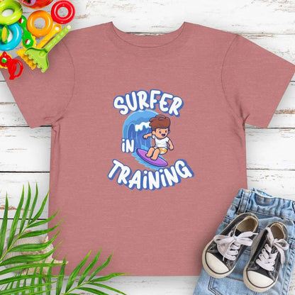 Surfer in Training Toddler's Heather Mauve T-shirt featuring a child surfing.