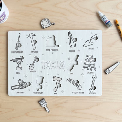 A wooden puzzle board with engraved tool shapes, including screwdriver, hammer, tape measure, pliers, trowel, drill, shovel, saw, ladder, chainsaw, paintbrush, axe, utility knife, and wrench, with several loose puzzle pieces placed nearby.