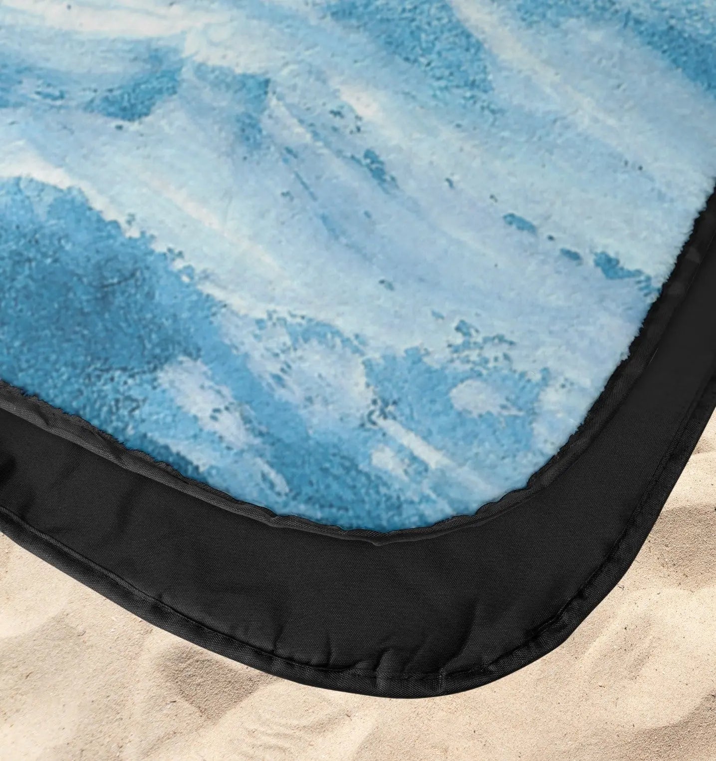 Corner of beach blanket showing graphic front and black waterproof back.
