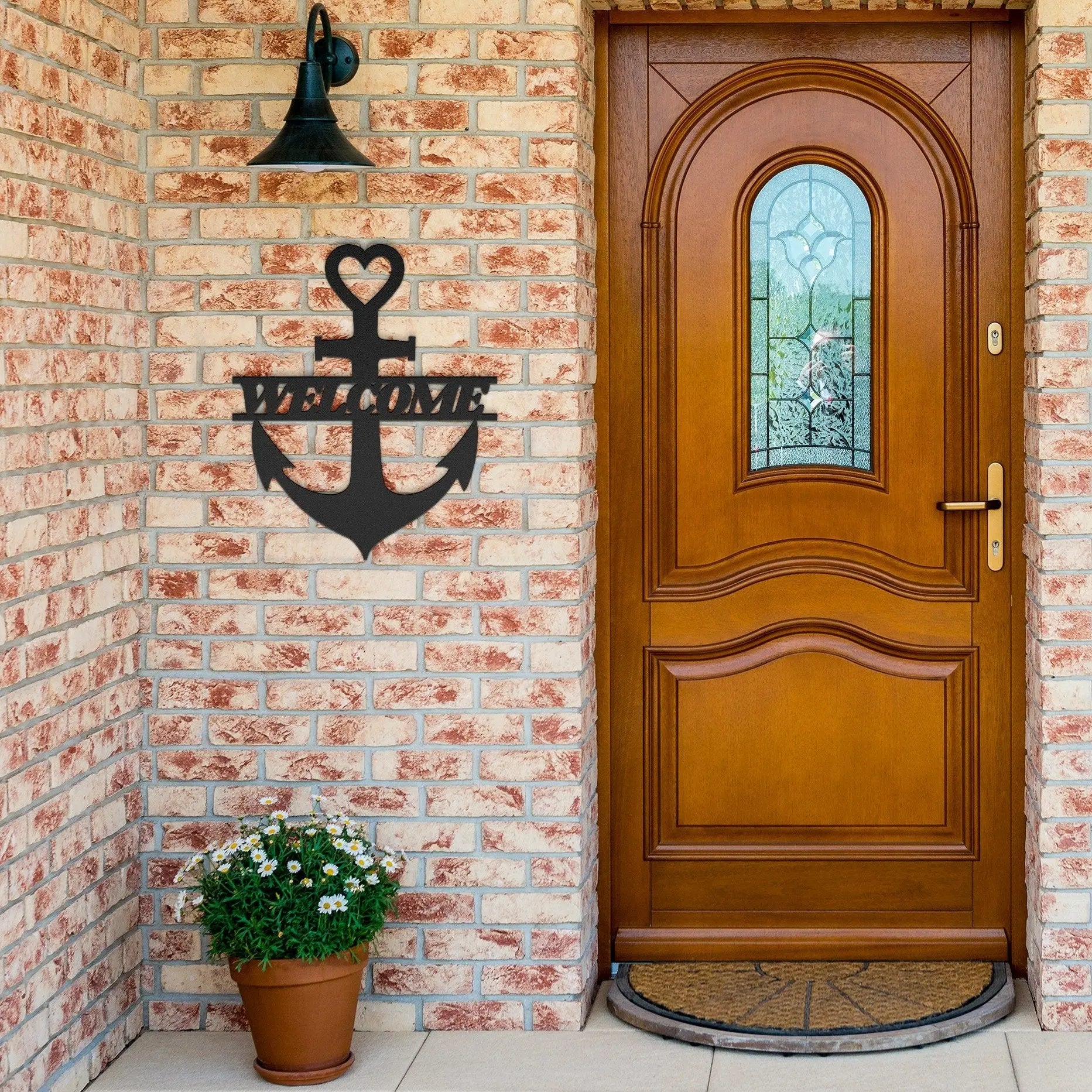 Black metal wall art shaped like an anchor with a heart at the top and the word “Welcome” cut out in the center; made of powder-coated steel hanging near the front door.