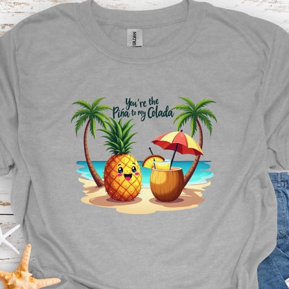 Gray T-shirt with a pineapple and a coconut pina colada on a beach between two palm trees with the text You're the Pina to my Colada.