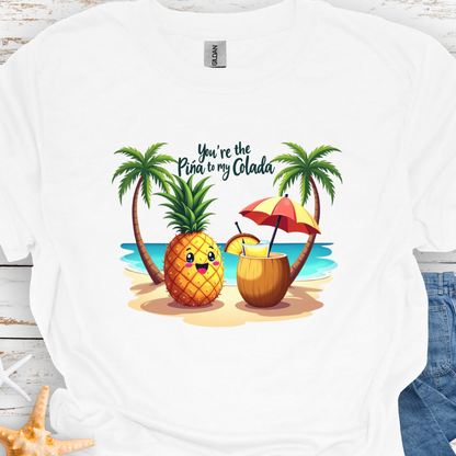 White T-shirt with a pineapple and a coconut pina colada on a beach between two palm trees with the text You're the Pina to my Colada.