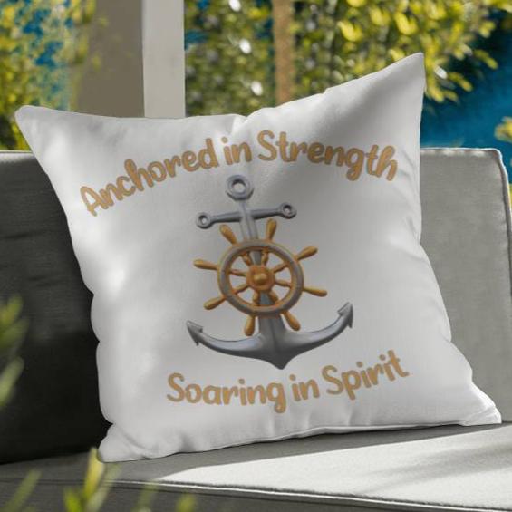 White pillow with a picture of an anchor and the words Anchored in Strength Soaring in Spirt surrounding sitting on a couch