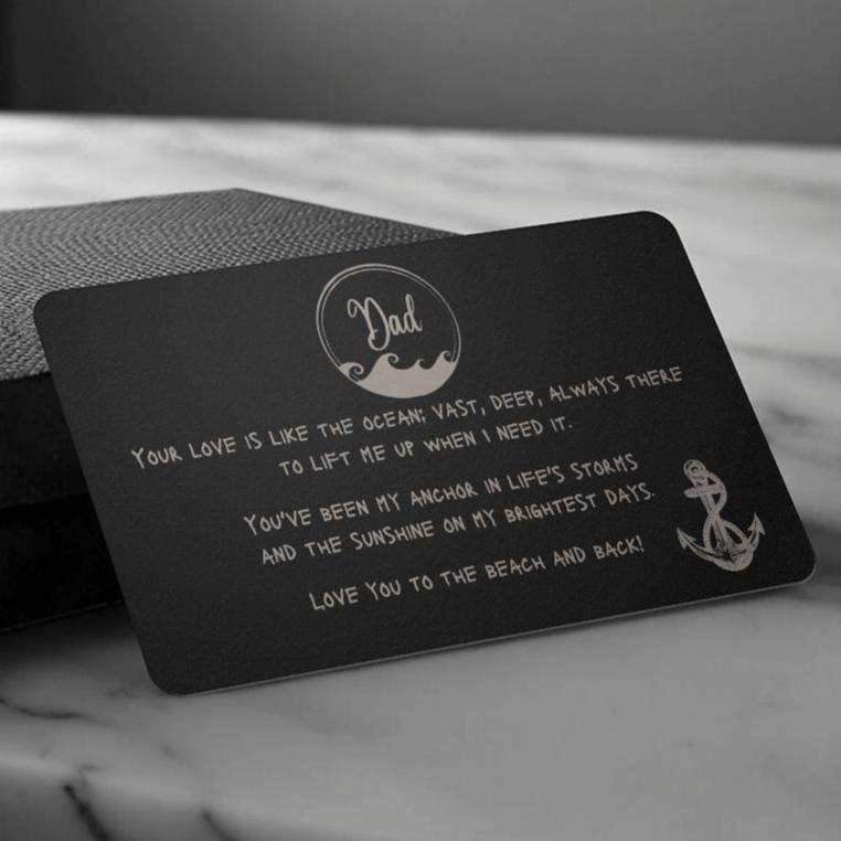 A black wallet sized stainless steel card that has a wave circle around the text dad and then says "your love is like the ocean; vast, deep, always there to lift me up when I need it. You've been my anchor in life's storms and the sunshine on my brightest days. Love you to the beach and back" and an image of an anchor on the bottom right side.