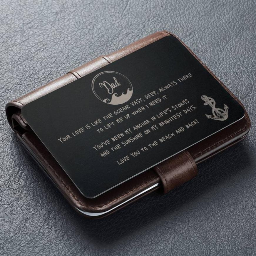 A black wallet sized stainless steel card that has a wave circle around the text dad and then says "your love is like the ocean; vast, deep, always there to lift me up when I need it. You've been my anchor in life's storms and the sunshine on my brightest days. Love you to the beach and back" and an image of an anchor on the bottom right side.