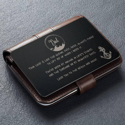 A black wallet sized stainless steel card that has a wave circle around the text dad and then says "your love is like the ocean; vast, deep, always there to lift me up when I need it. You've been my anchor in life's storms and the sunshine on my brightest days. Love you to the beach and back" and an image of an anchor on the bottom right side.