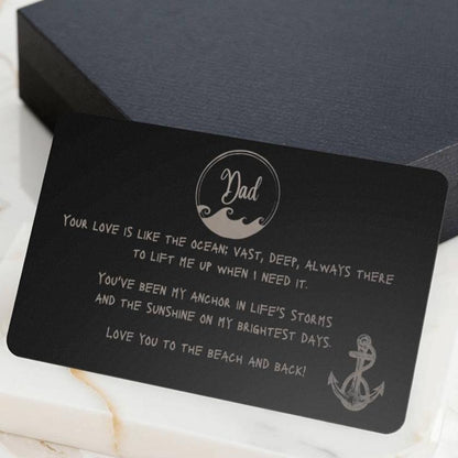 A black wallet sized stainless steel card that has a wave circle around the text dad and then says "your love is like the ocean; vast, deep, always there to lift me up when I need it. You've been my anchor in life's storms and the sunshine on my brightest days. Love you to the beach and back" and an image of an anchor on the bottom right side.