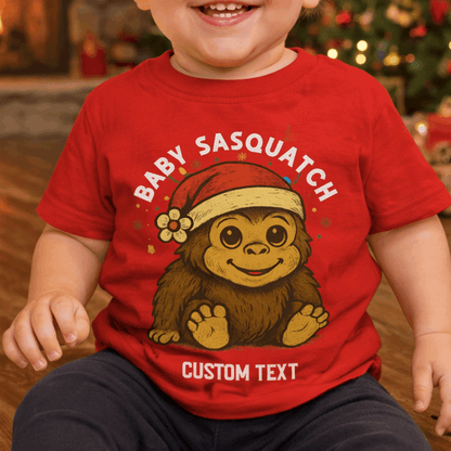 Child wearing a red 'Baby Sasquatch' t-shirt with a Christmas-themed design.