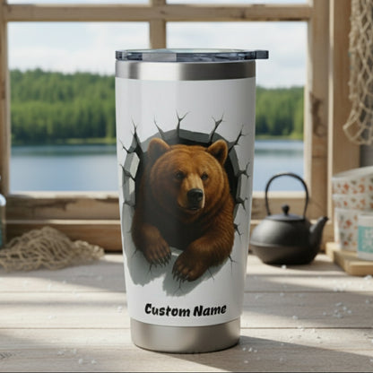 Stainless steel tumbler with bear design on a wooden surface with a window view of trees and water.