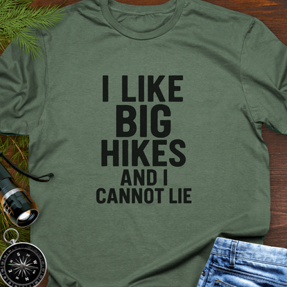 Green t-shirt with 'I LIKE BIG HIKES AND I CANNOT LIE' text, surrounded by hiking accessories on a wooden surface.