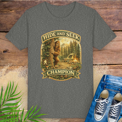 Gray t-shirt with 'Hide and Seek Champion' graphic with Bigfoot peeking around a tree in a campsite.