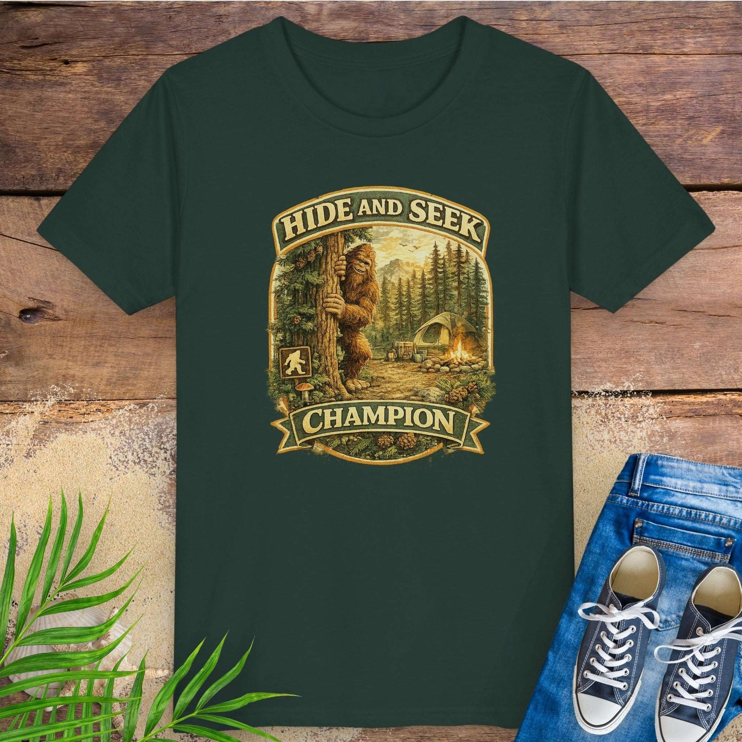 Green t-shirt with 'Hide and Seek Champion' graphic with Bigfoot peeking around a tree in a campsite.