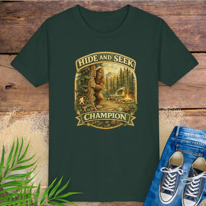 Green t-shirt with 'Hide and Seek Champion' graphic with Bigfoot peeking around a tree in a campsite.