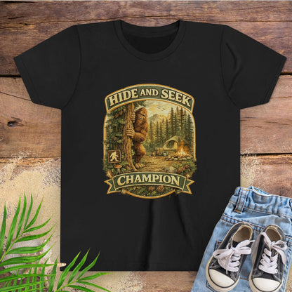 Black t-shirt with 'Hide and Seek Champion' graphic on a wooden surface with sneakers and leaves.