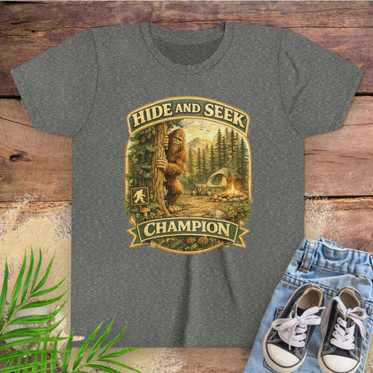 Gray t-shirt with 'Hide and Seek Champion' graphic on a wooden surface with sneakers and leaves.