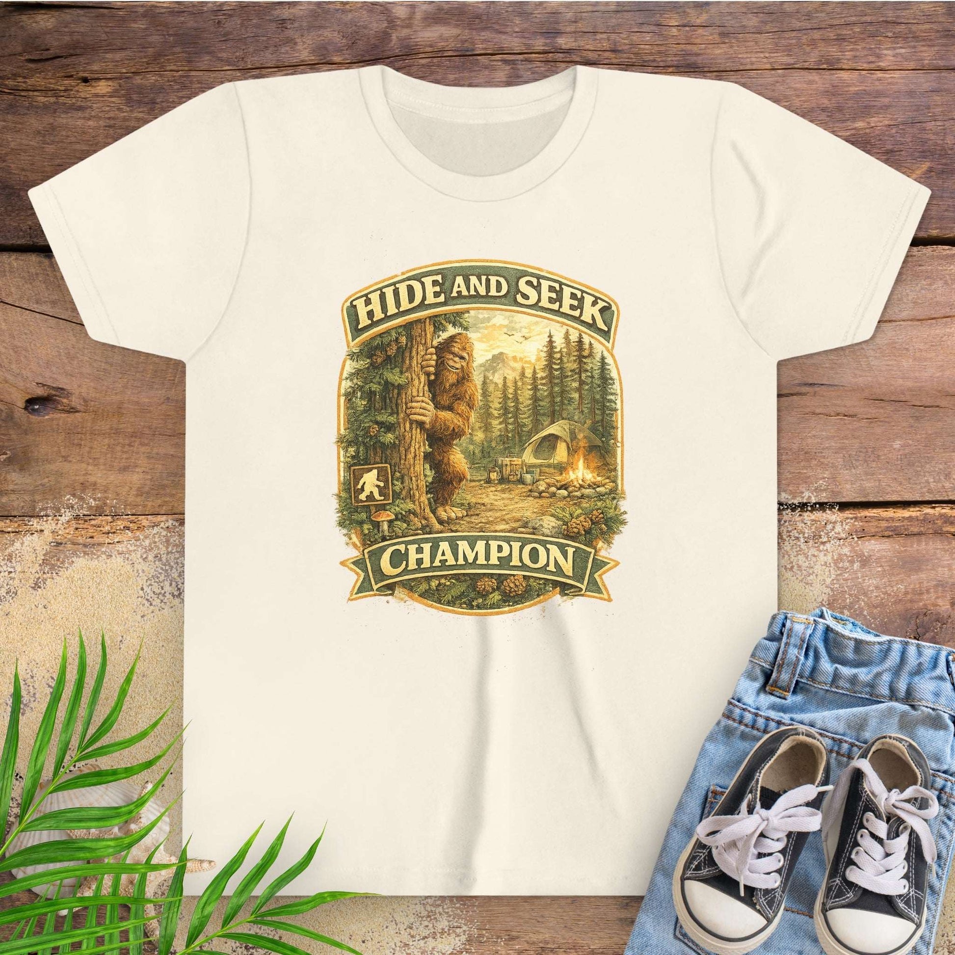 Beige t-shirt with 'Hide and Seek Champion' graphic on a wooden surface with blue jeans and sneakers.