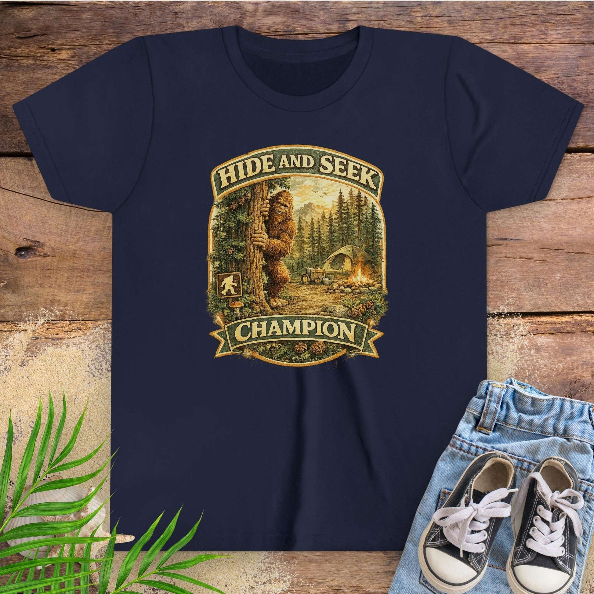 Navy blue t-shirt with 'Hide and Seek Champion' graphic on a wooden surface with sneakers and jeans.