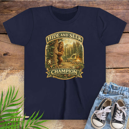Navy blue t-shirt with 'Hide and Seek Champion' graphic on a wooden surface with sneakers and jeans.