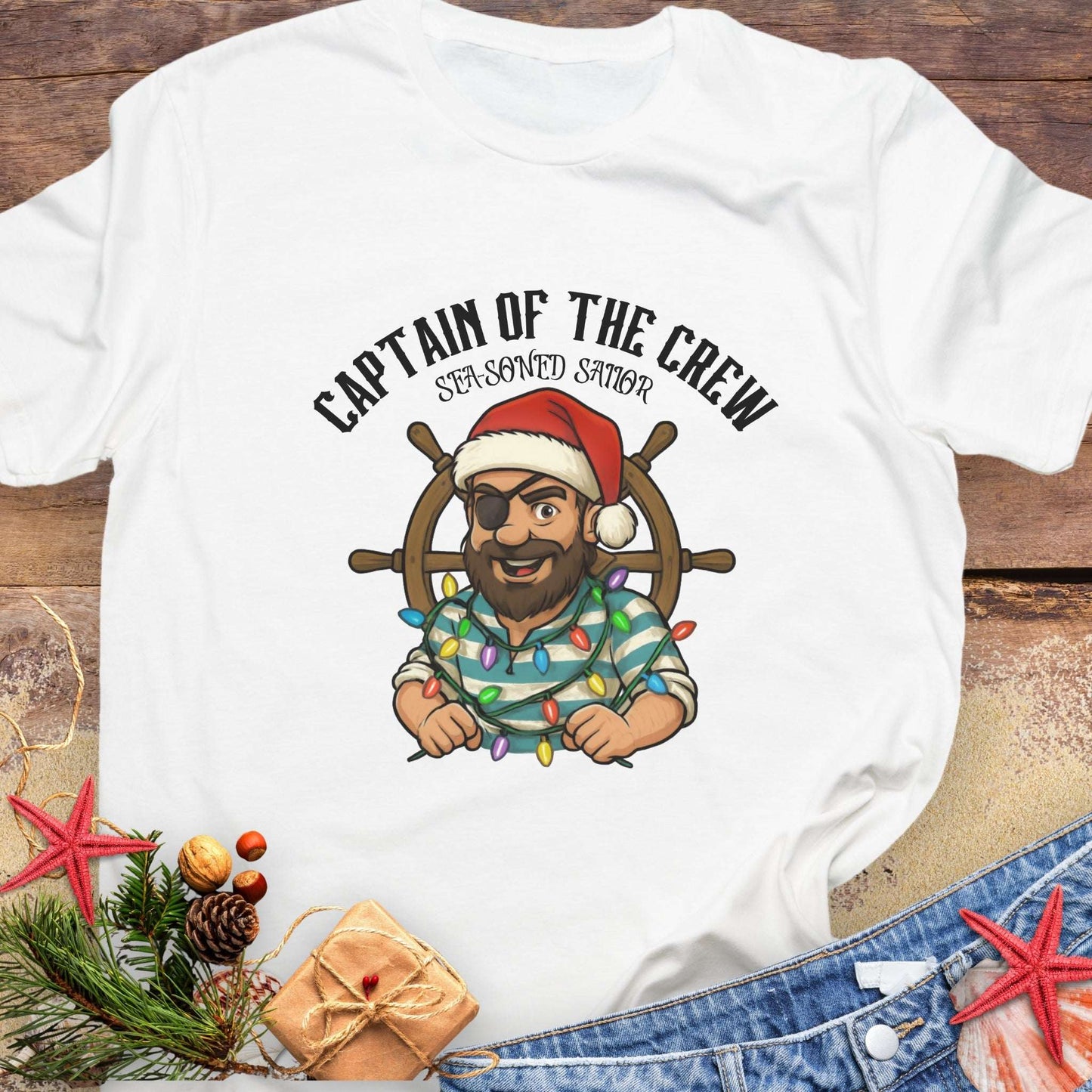 White t-shirt with a cartoon pirate wearing a Santa hat and 'Captain of the Crew' text on a wooden surface.